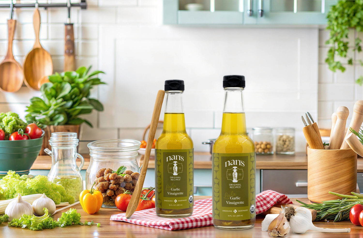 two bottles of nans vinaigrette on a brightly lit wooden kitchen counter surrounded by ingredients with a wooden spoon leaning against one of the bottles